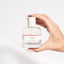 A hand holding a 50ml bottle of custom scent eau de parfum with a white label and red accents on the bottle.